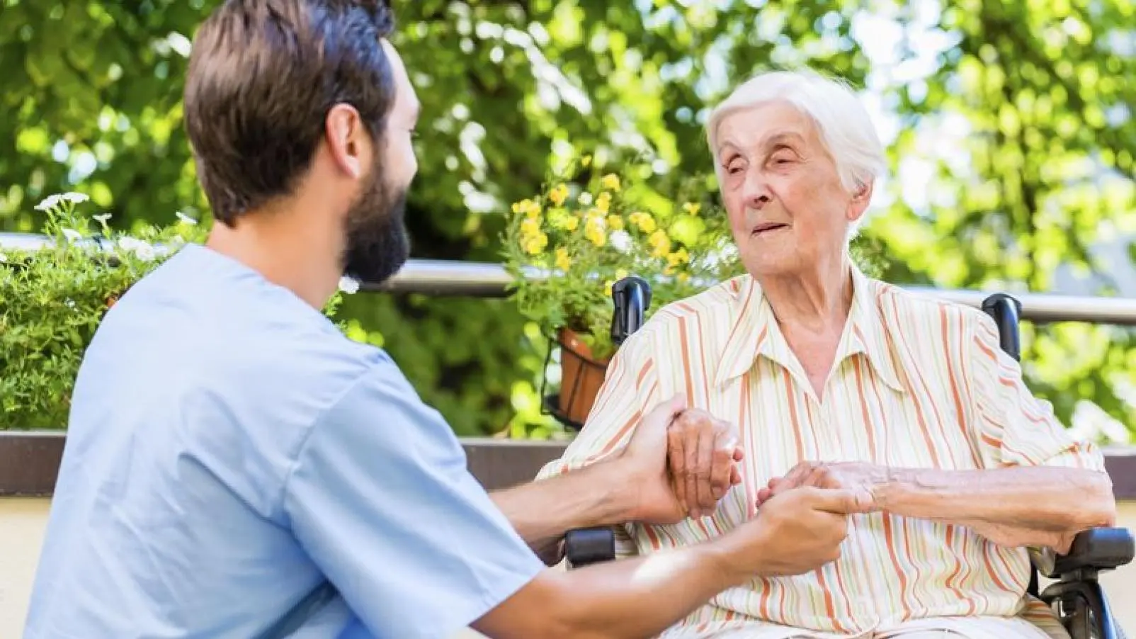 Young male caregiver holding hands with an elderly woman in a wheelchair